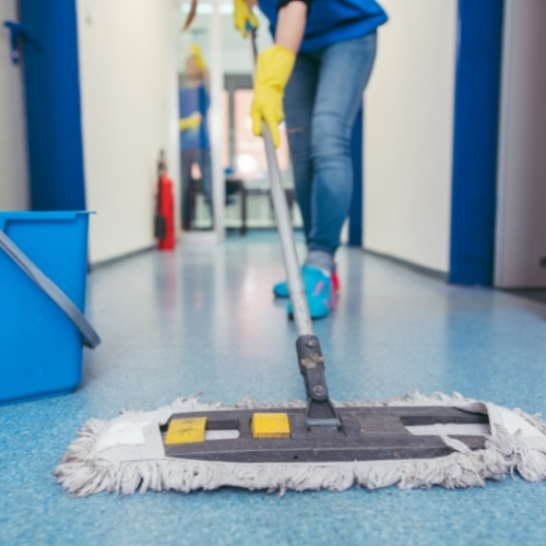 janitor holding a mop performing mopping along a corridor of a building