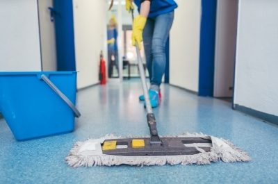 a cleaner mopping the blue flooring of a corridor in a building
